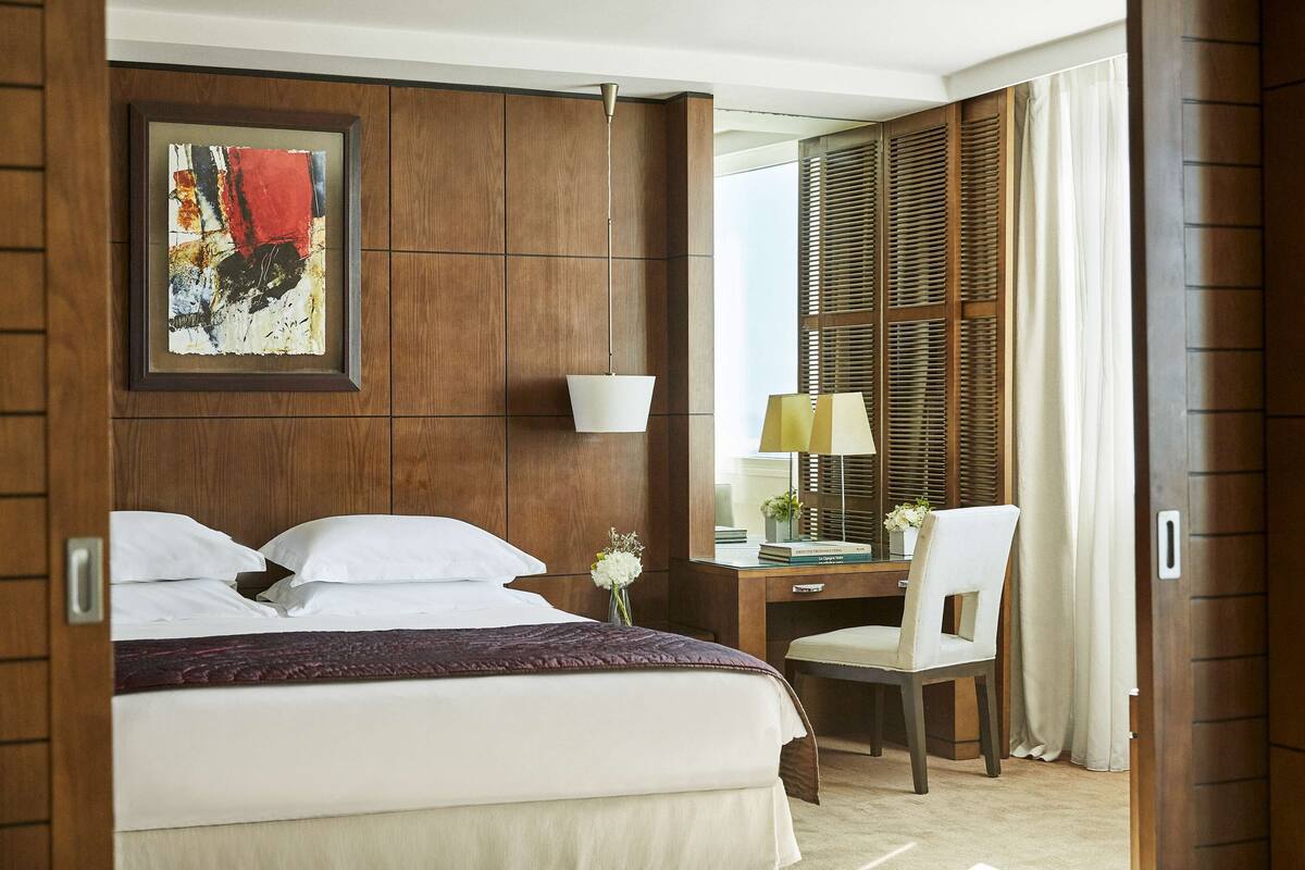 Une chambre d’hôtel comprenant un lit, un bureau avec une chaise, une lampe, un miroir et une armoire.