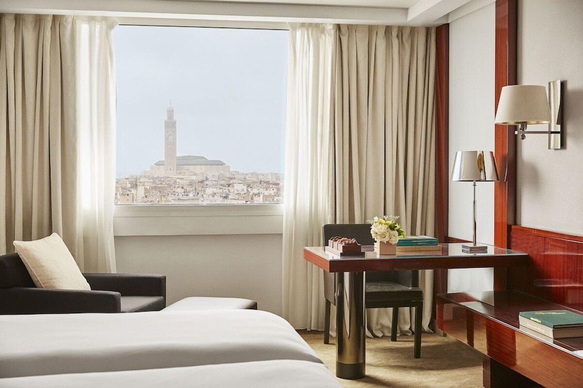 A hotel room with a bed, a desk, a chair, and a view of a cityscape.