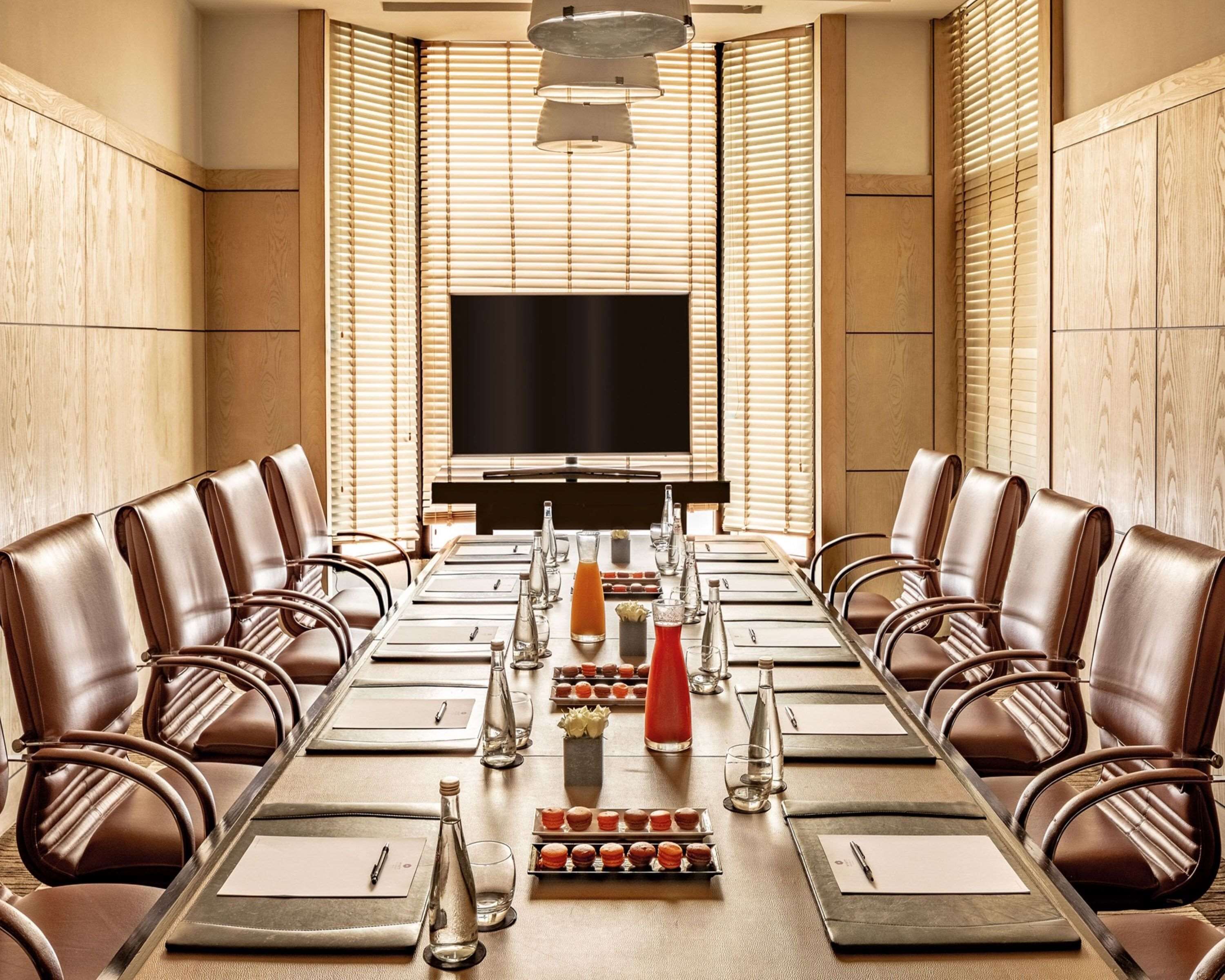 A conference room with a long table, leather chairs, a large screen, and a wooden paneled wall.