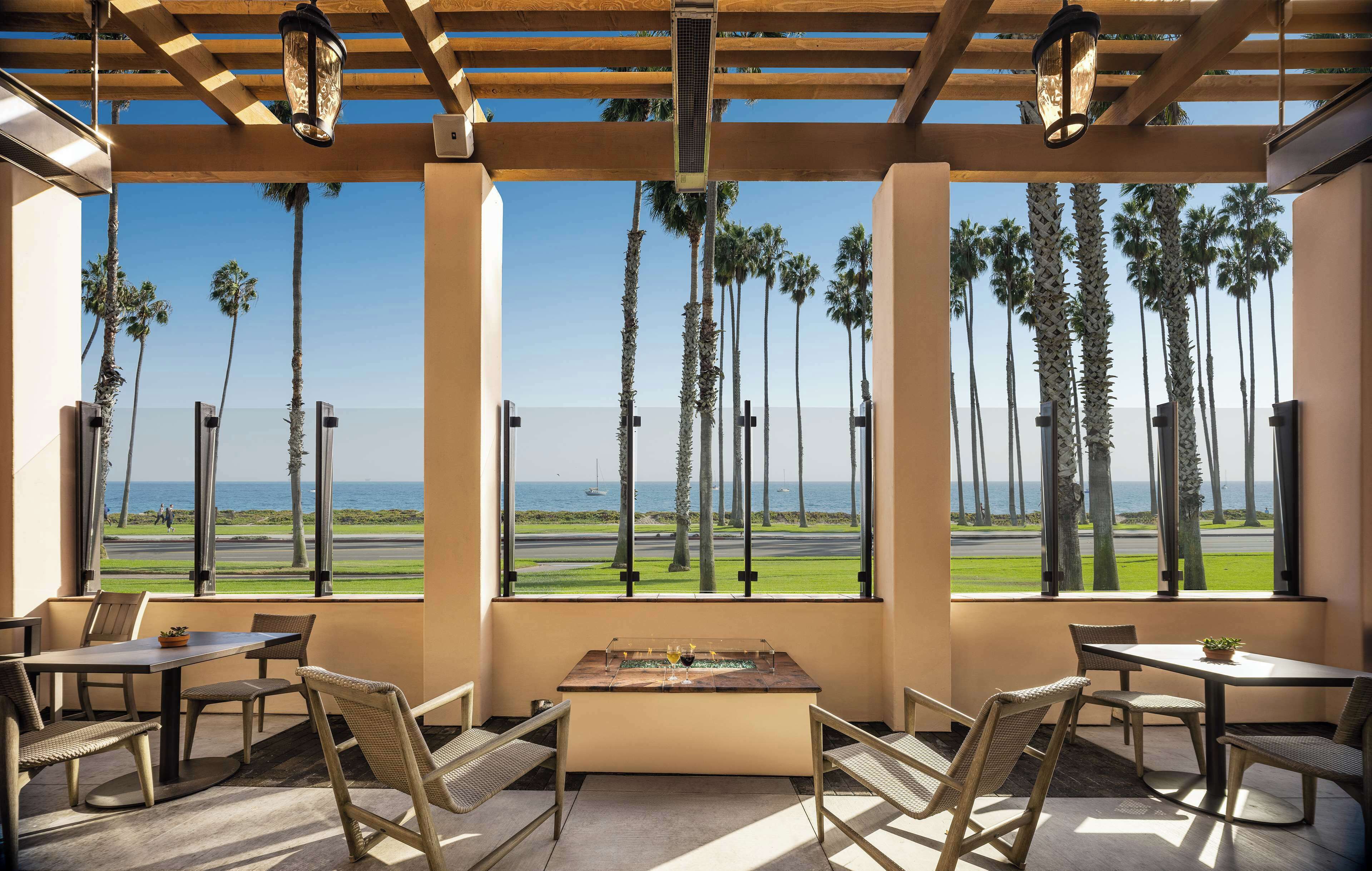 A covered outdoor seating area with tables and chairs, overlooking a runway and palm trees.