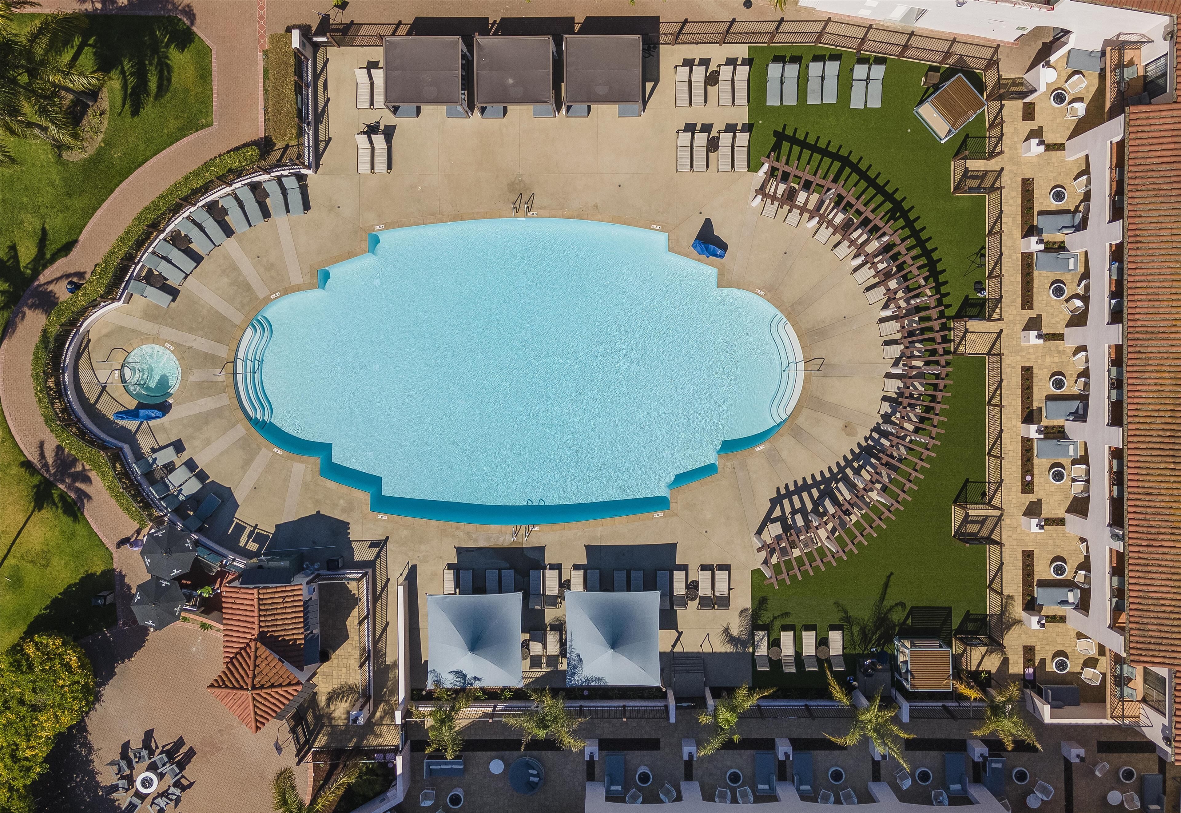 Vista aérea de un complejo turístico con una piscina central, sillas de descanso y una zona de estar circular.