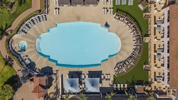 Vista aérea de un complejo turístico con una piscina central, sillas de descanso y una zona de estar circular.