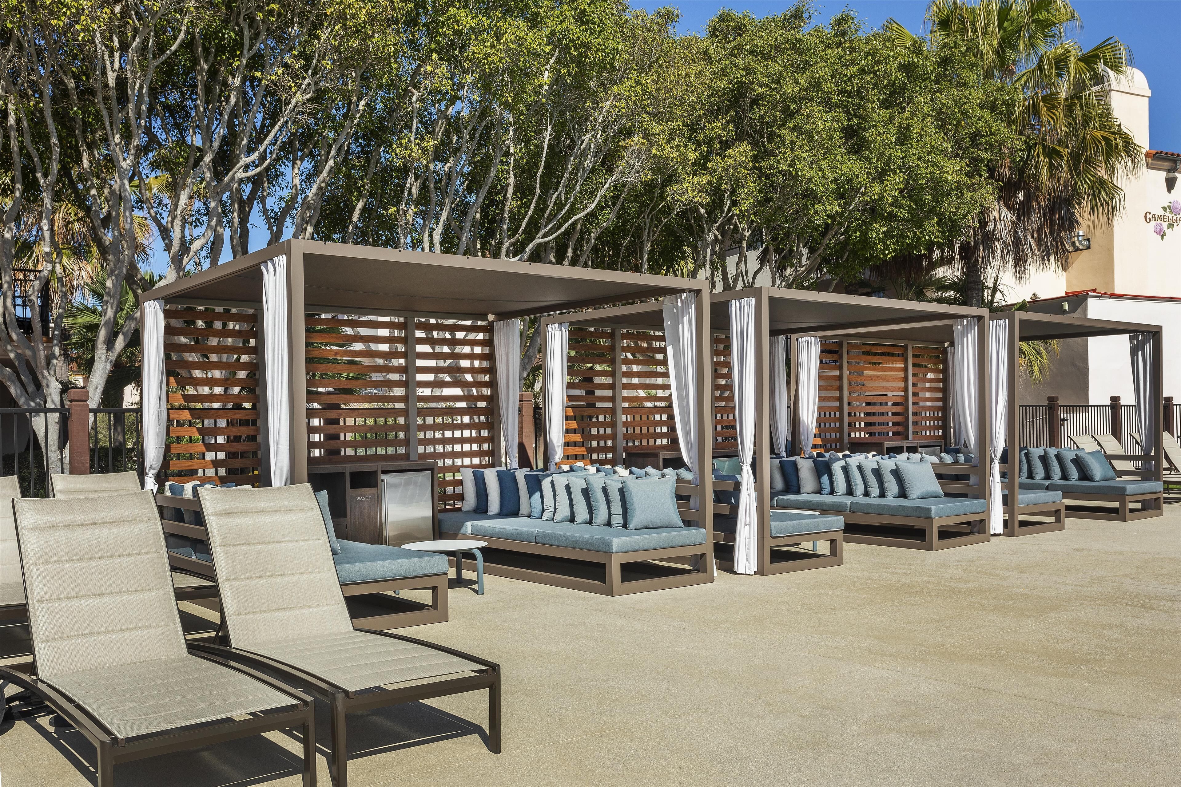 Espace extérieur aménagé avec des chaises et des canapés confortables, une zone couverte avec des lambris en bois et un décor composé d’arbres.