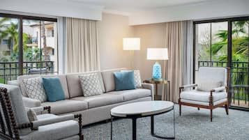 A hotel room with a beige sofa, a wooden armchair, a round coffee table, and a lamp.