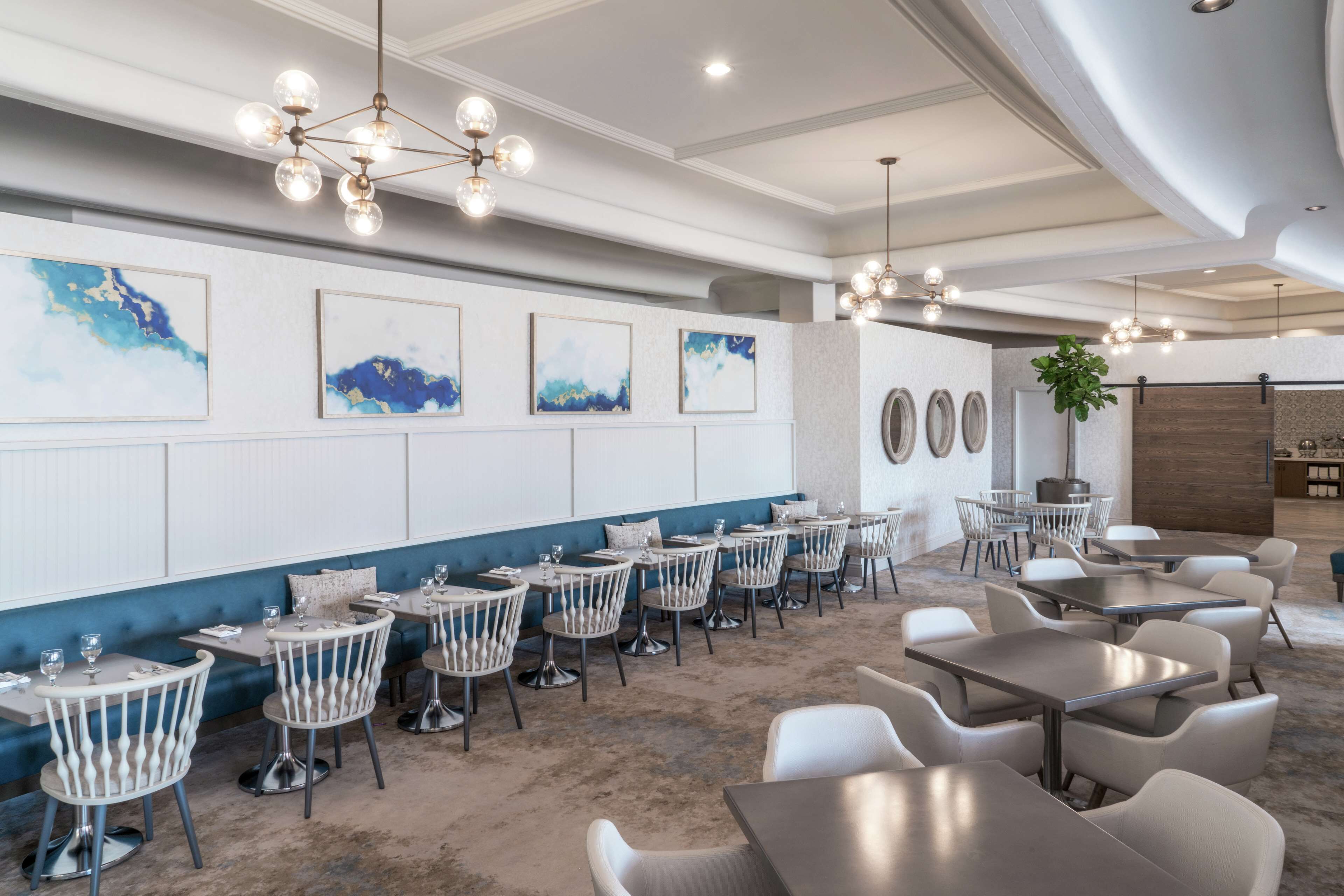 A modern dining area with round tables and chairs, a blue accent wall, and abstract art.