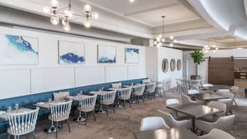 A modern dining area with round tables and chairs, a blue accent wall, and abstract art.
