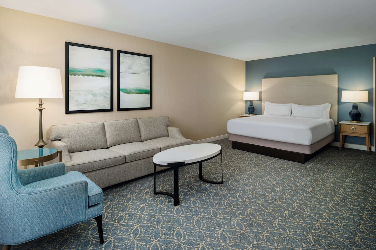 A hotel room with a bed, a sofa, a small table, and two wall-mounted lamps.