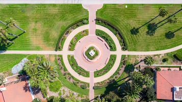 Vista aérea de um cruzamento ajardinado com um monumento circular central, cercado por vegetação e palmeiras.