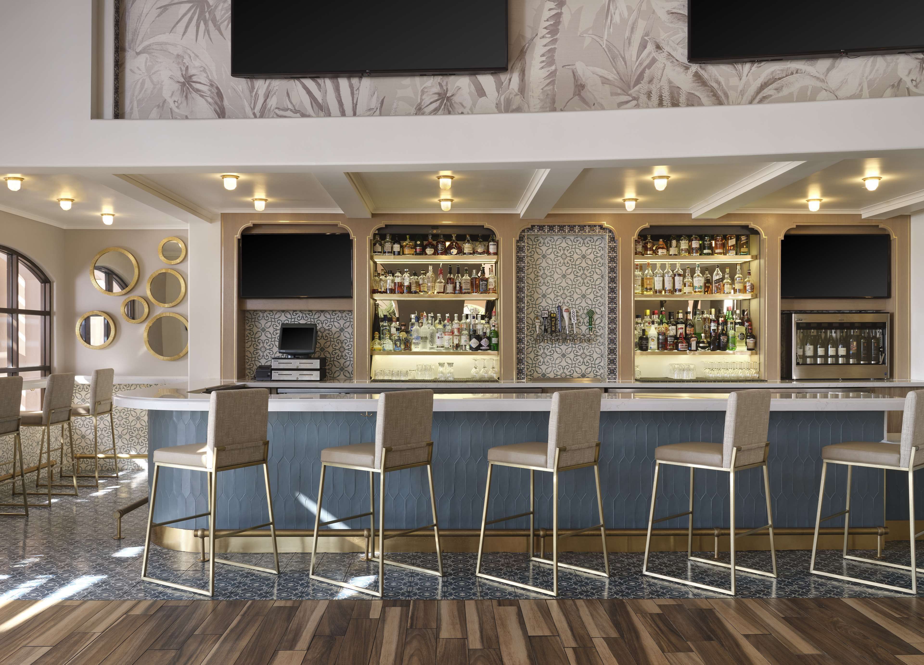 Uma área de bar com balcão, banquetas e prateleiras cheias de garrafas de bebidas.