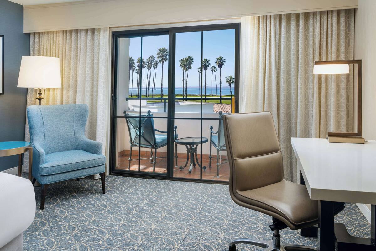 A hotel room with a balcony, two chairs, a table, and a lamp.