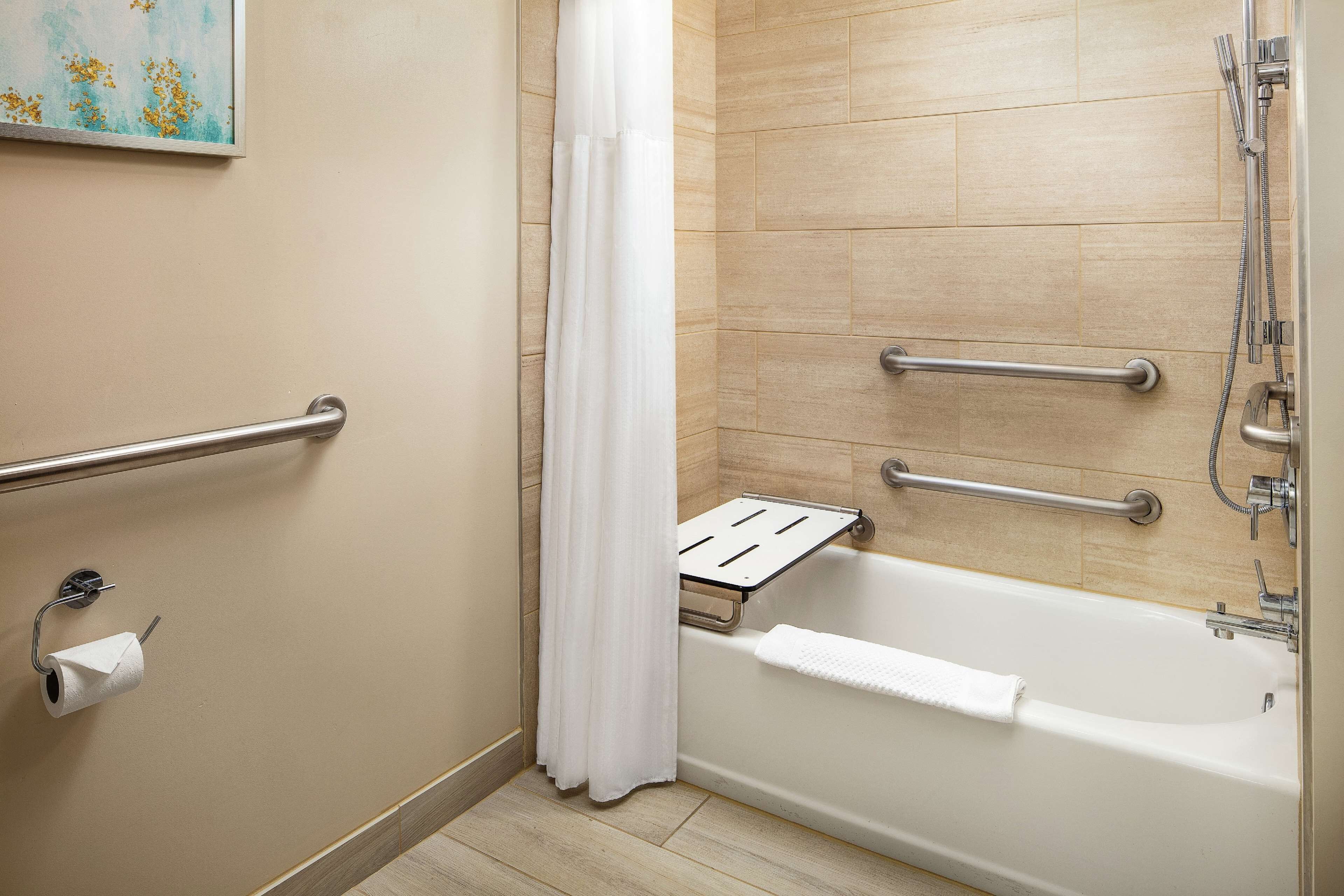 A bathroom with a bathtub, a shower, and a toilet with a handrail.