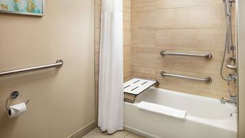 A bathroom with a bathtub, a shower, and a toilet with a handrail.
