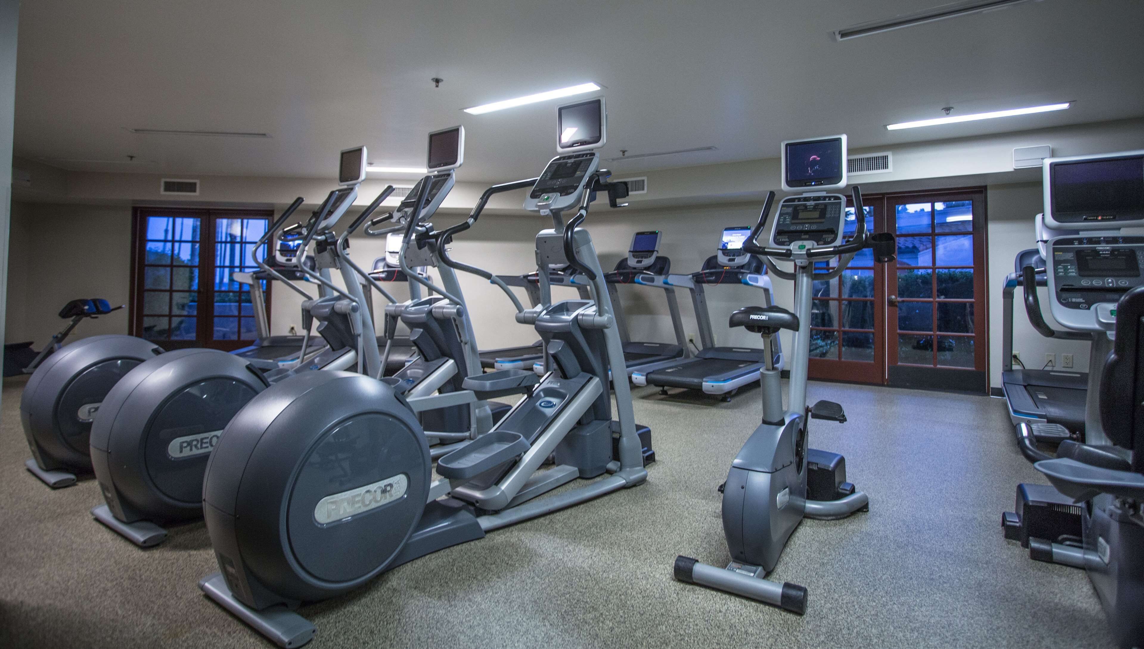 A gym with various exercise machines, including treadmills and elliptical trainers, arranged in rows.