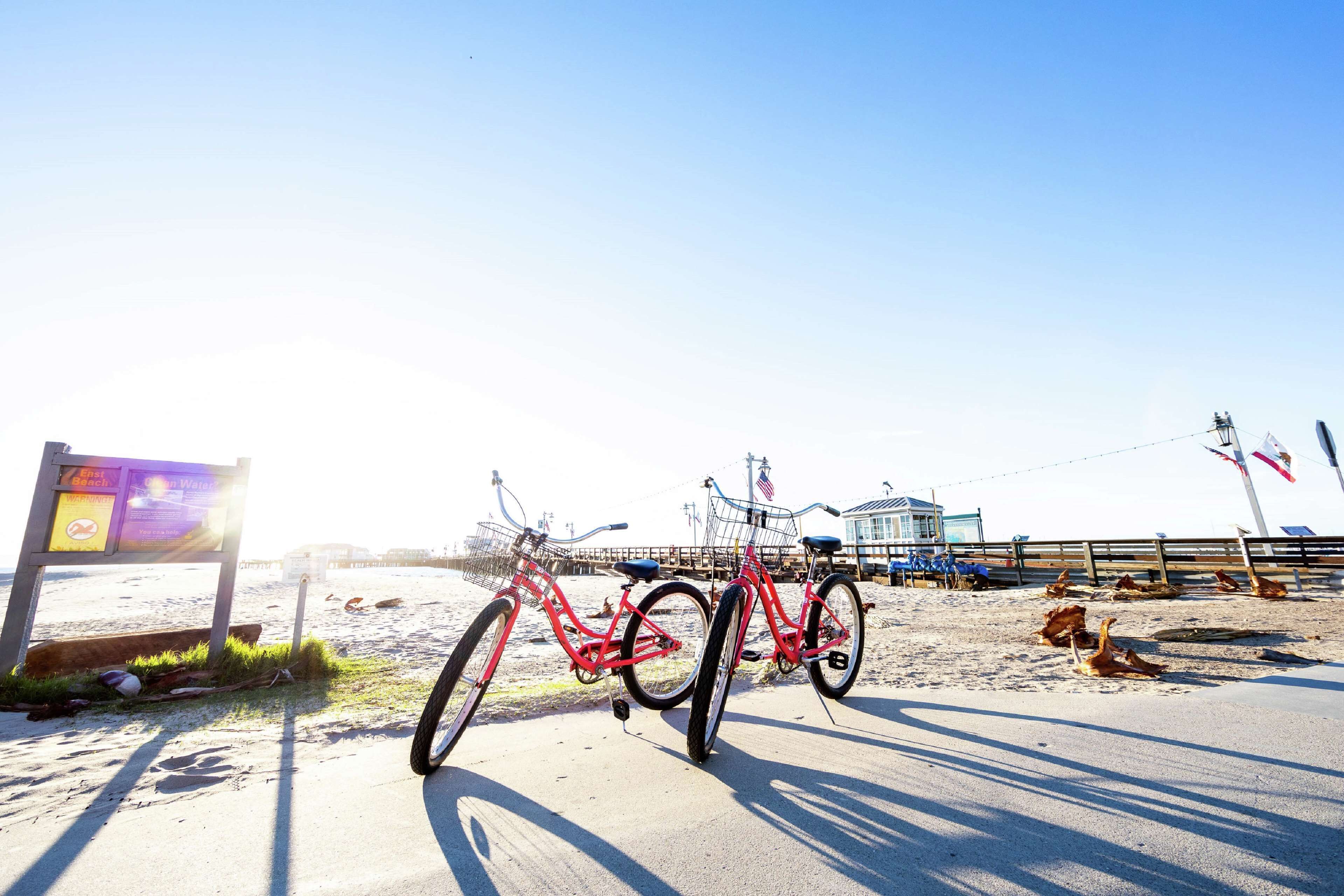 A beachside bicycle rental station with a sign indicating a beach and a pier in the background.