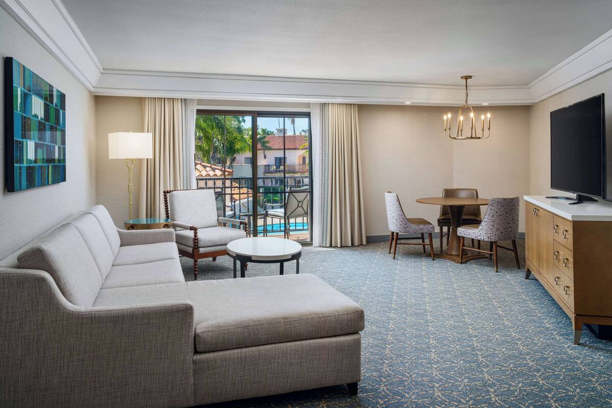 A hotel room with a sofa, two chairs, a small table, a TV, and a balcony with a pool view.