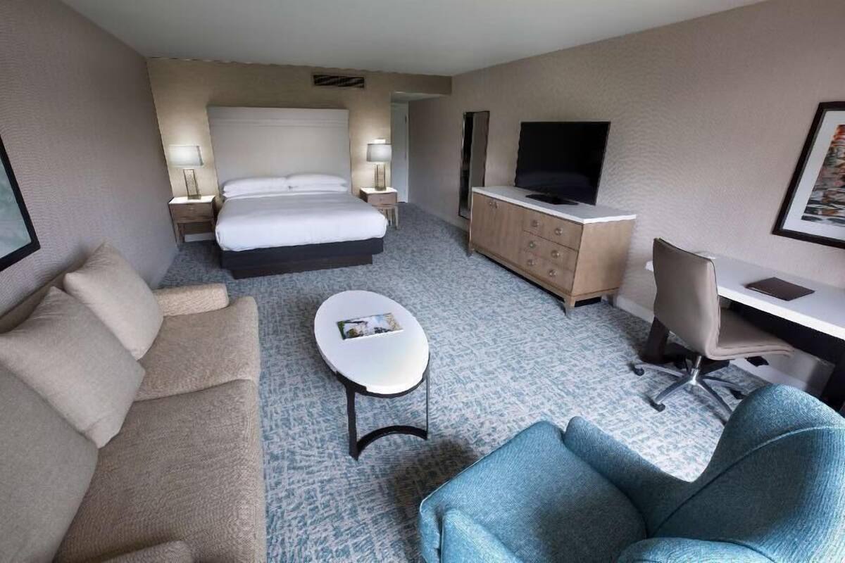 A hotel room with a bed, a desk, a TV, a sofa, and a small table.