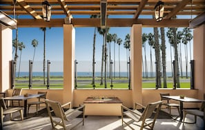 A covered outdoor seating area with tables and chairs, overlooking a runway and palm trees.