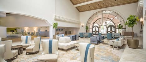 Un vestíbulo amplio con mobiliario moderno, techo alto y un gran ventanal de arco.