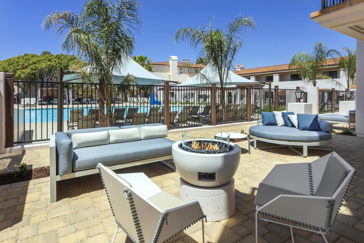 A poolside area with lounge chairs, a fire pit, and a view of the pool and building.