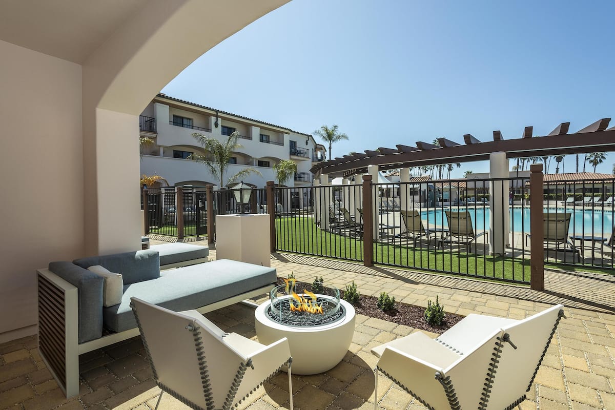 A patio area with outdoor seating, a fire pit, and a view of a pool and building in the background.
