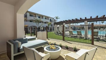 Un patio con mobiliario exterior, una fogata y vistas a una piscina y un edificio al fondo.