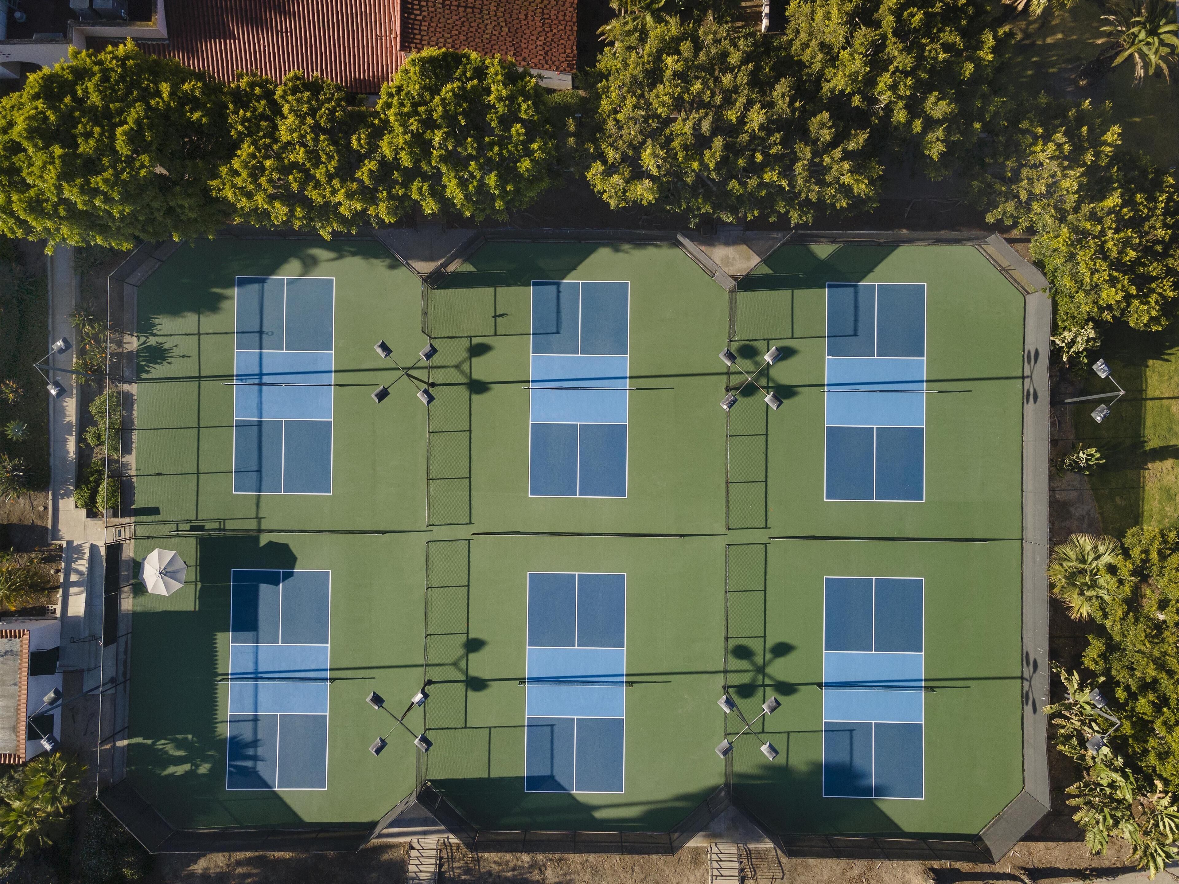 An aerial view of a tennis court complex with multiple courts, surrounded by trees and buildings.