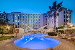 Een hotel met een zwembad, ligbedden en een palmboom.