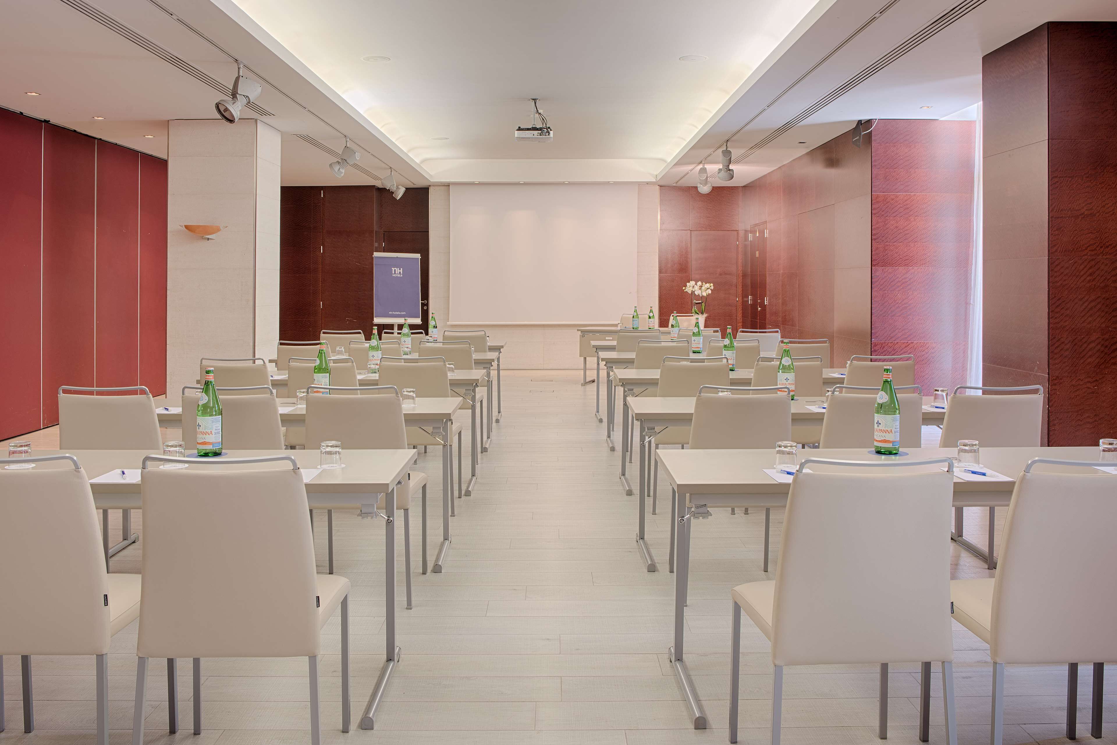 A conference room with rows of tables and chairs, equipped with projectors and screens, and a large whiteboard.