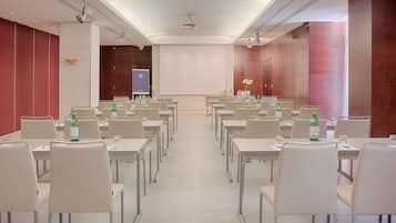 A conference room with rows of tables and chairs, equipped with projectors and screens, and a large whiteboard.
