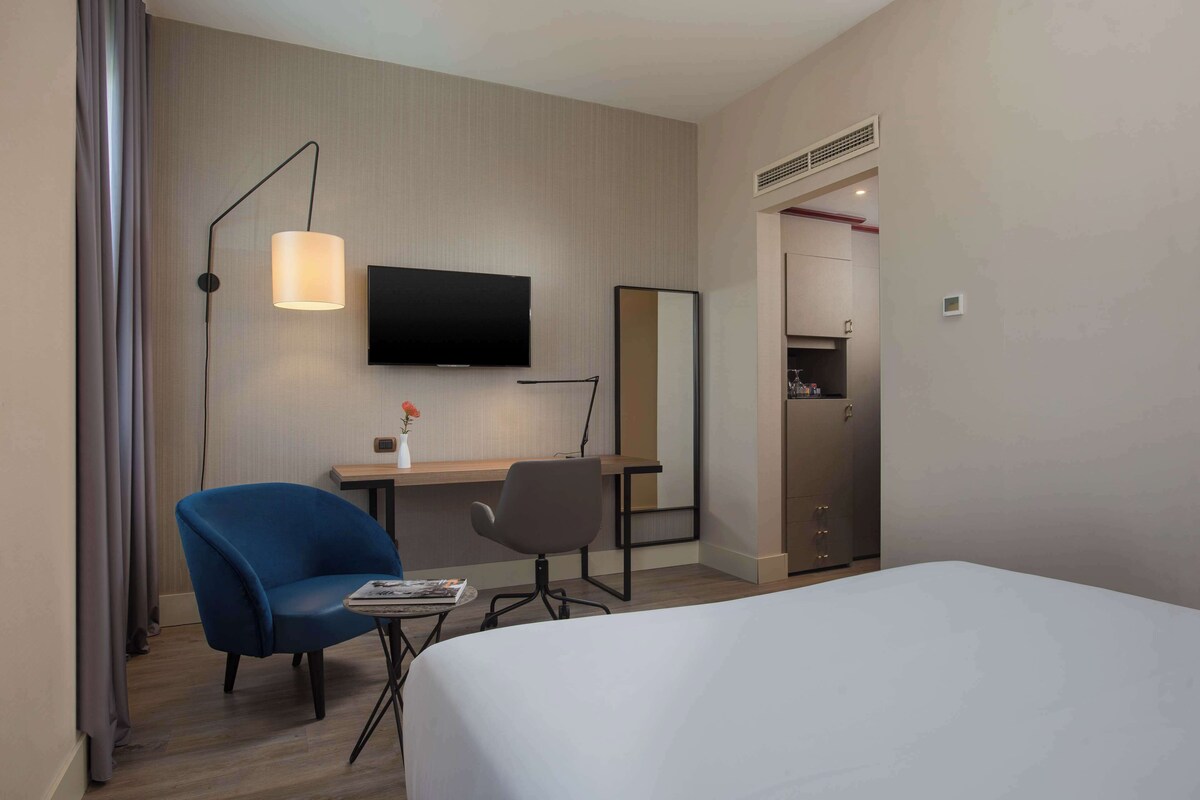 Een hotelkamer met een bed, een bureau met stoel, een televisie, een spiegel en een kledingkast.