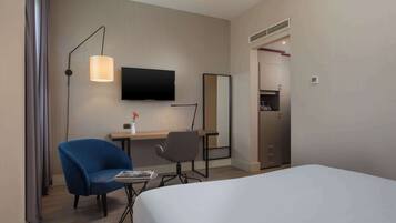 Ein Hotelzimmer mit Bett, Schreibtisch mit Stuhl, Fernseher, Spiegel und Kleiderschrank.