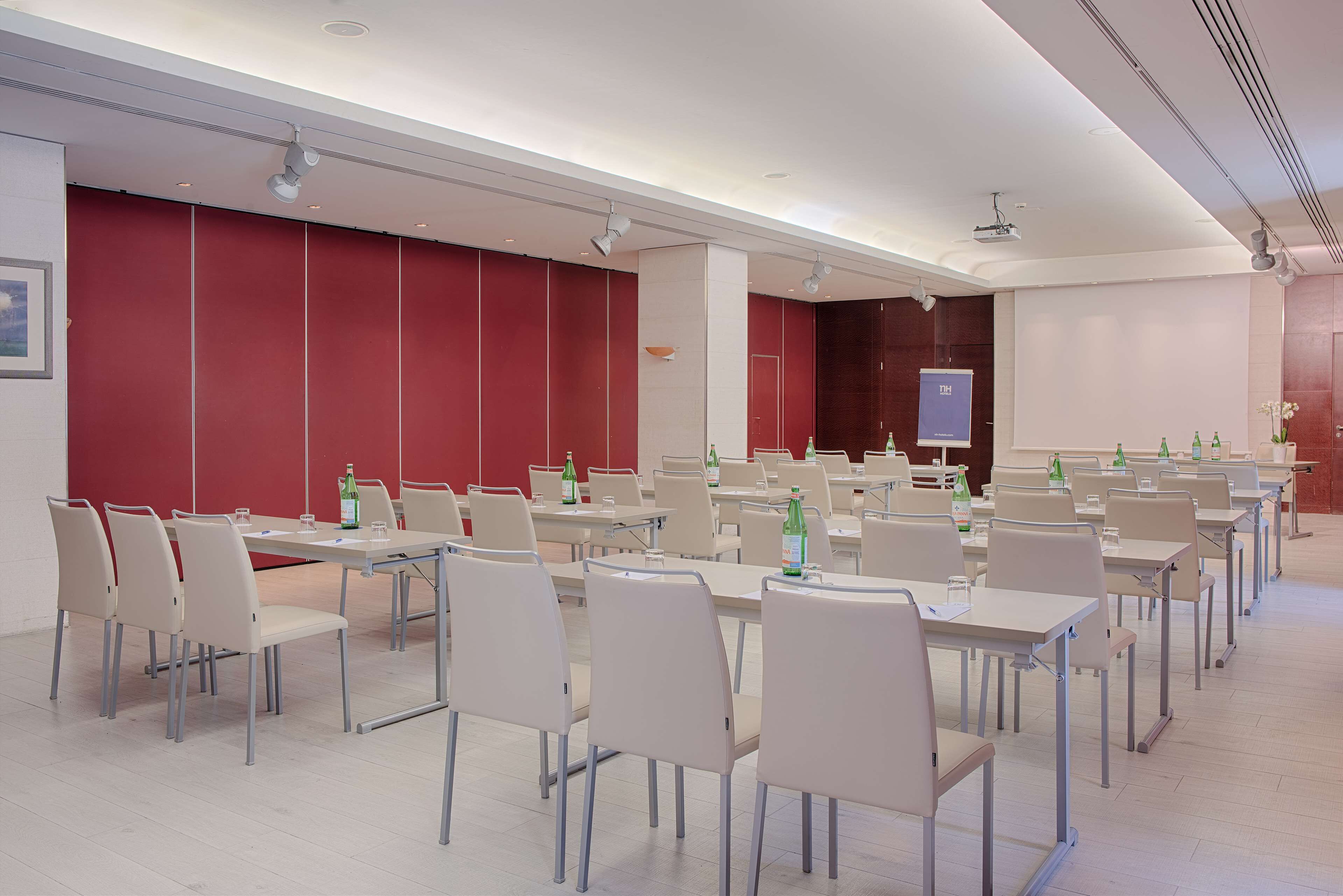 Une salle de conférence équipée de plusieurs tables et chaises, d’un écran de projection et d’un tableau blanc.