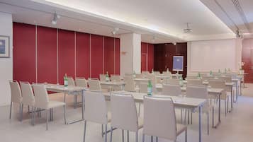 A conference room with multiple tables and chairs, a projector screen, and a whiteboard.
