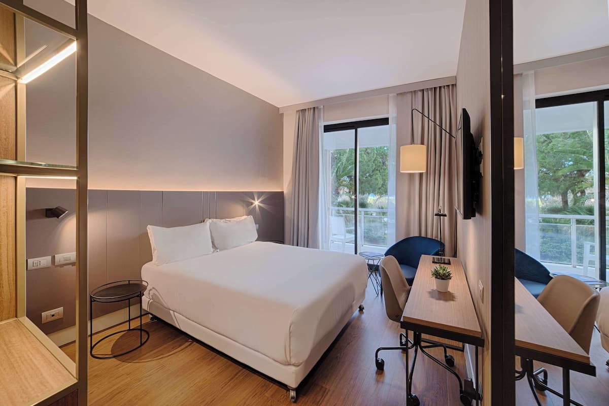 A hotel room with a large bed, a desk, a chair, a TV, and a window with curtains.