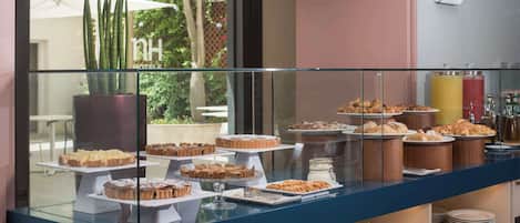 Un mostrador de buffet con diversos postres y pasteles, una vitrina de cristal y vistas a un jardín por la ventana.