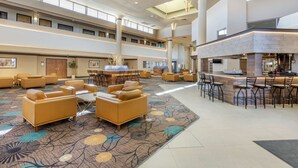 A spacious lobby with multiple seating areas, a central bar, and a high ceiling with skylights.