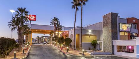 A hotel entrance with a sign reading "Best Western PLUS," palm trees, and a well-lit parking area.