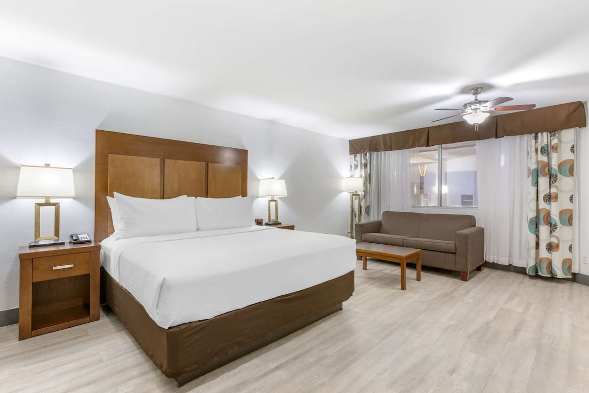 Een hotelkamer met een groot bed, een bank, een tafeltje en een plafondventilator.