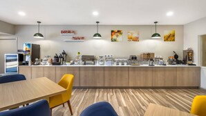 A modern kitchen area with a wooden countertop, various appliances, and a seating area with blue and yellow chairs.