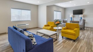 A modern living room with a blue sofa, yellow armchairs, a coffee table, and a flat-screen TV mounted on the wall.