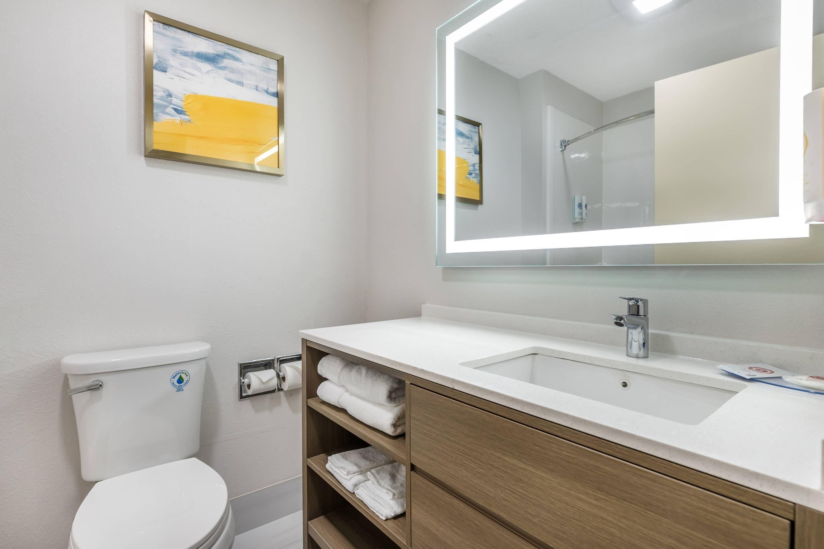 Un baño moderno con inodoro blanco, lavamanos con espejo y estante con toallas.