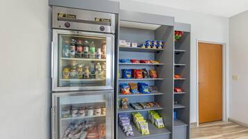Uma cozinha compacta com um refrigerador cheio de bebidas e lanches, um micro-ondas e um pequeno armário com alimentos embalados.