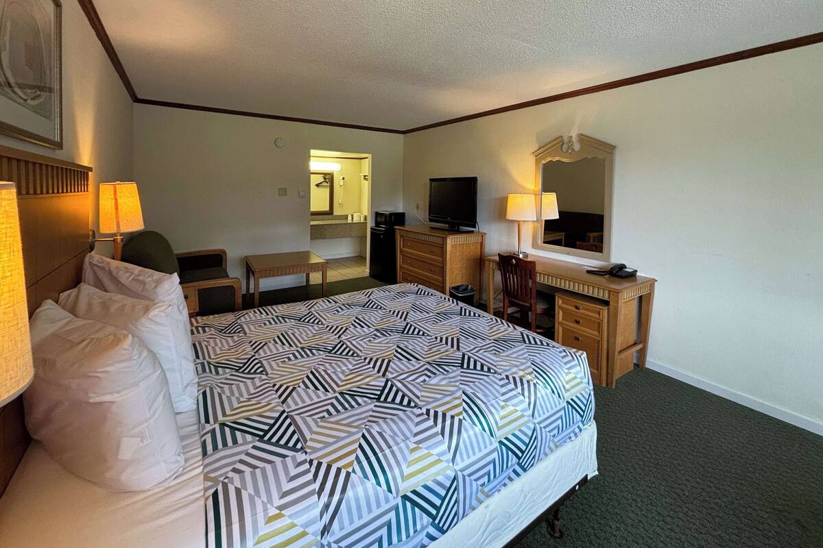 A hotel room with a bed, desk, chair, dresser, television, and a mirror.