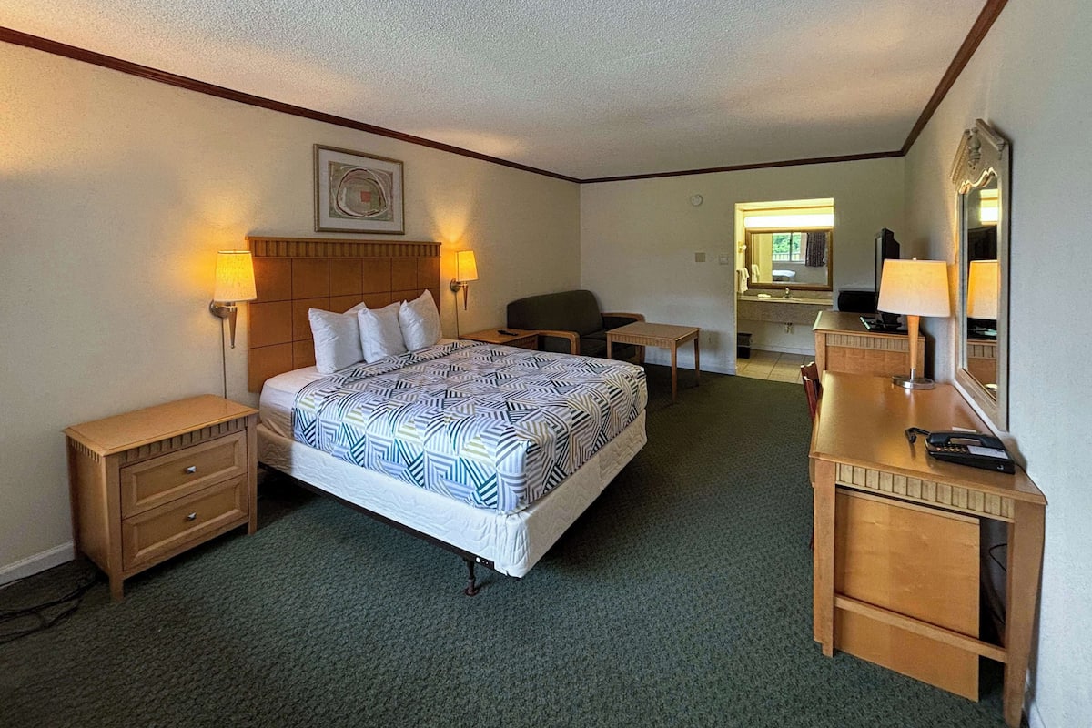A hotel room with a large bed, two bedside tables, a desk with a chair, a small table, and a mirror.