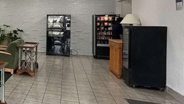 Un'area di accoglienza con pavimento piastrellato, una macchina distributrice, un frigorifero e una lampada.