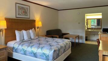 Ein Hotelzimmer mit Bett, zwei Nachttischlampen, einem Sessel, einem kleinen Tisch, einem Spiegel und einem Fenster.
