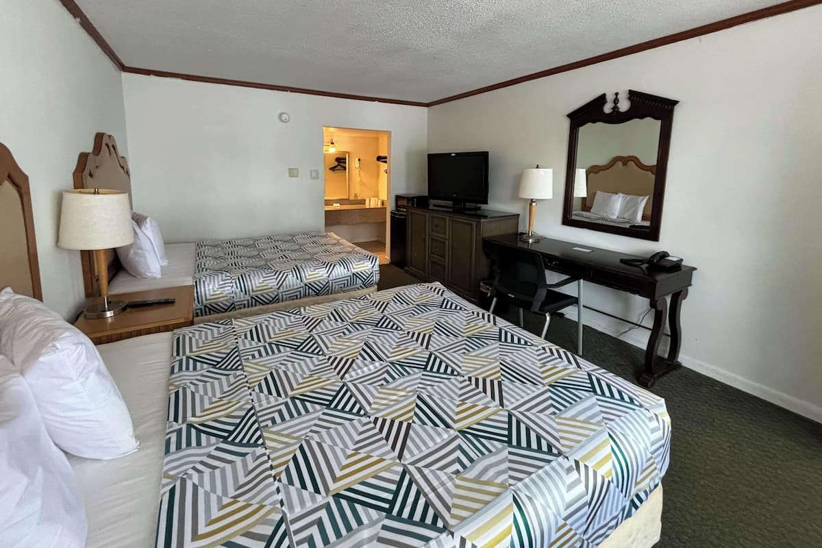 A hotel room with two beds, a desk, a television, a mirror, and a bathroom visible through an open door.