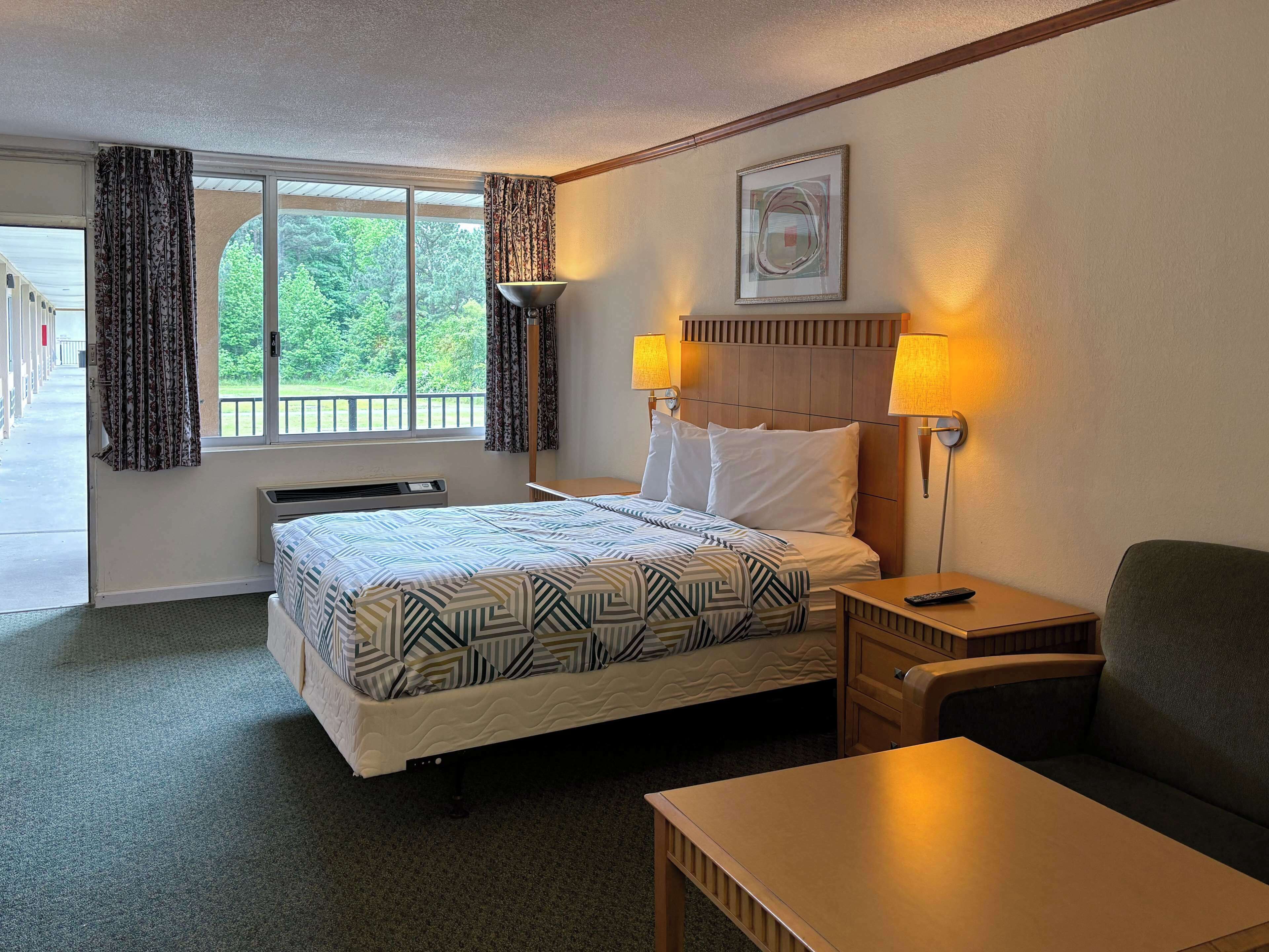 A hotel room with a bed, bedside table, chair, and a window with curtains.