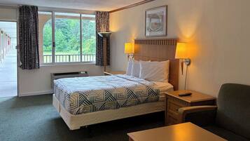 A hotel room with a bed, bedside table, chair, and a window with curtains.