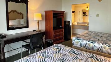Habitación de hotel con escritorio, dos camas, espejo, lámpara, armario, cubo de basura y kitchenette.